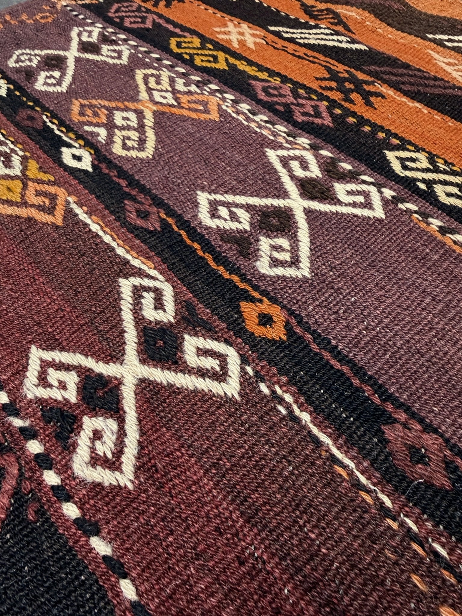Close-up of a patterned fabric with geometric designs in brown, black, and white. Vintage Kars kilim rug from Eastern Turkey, 6 x 8, with horizontal tribal bands in brown, ivory, rust, and charcoal geometric motifs.