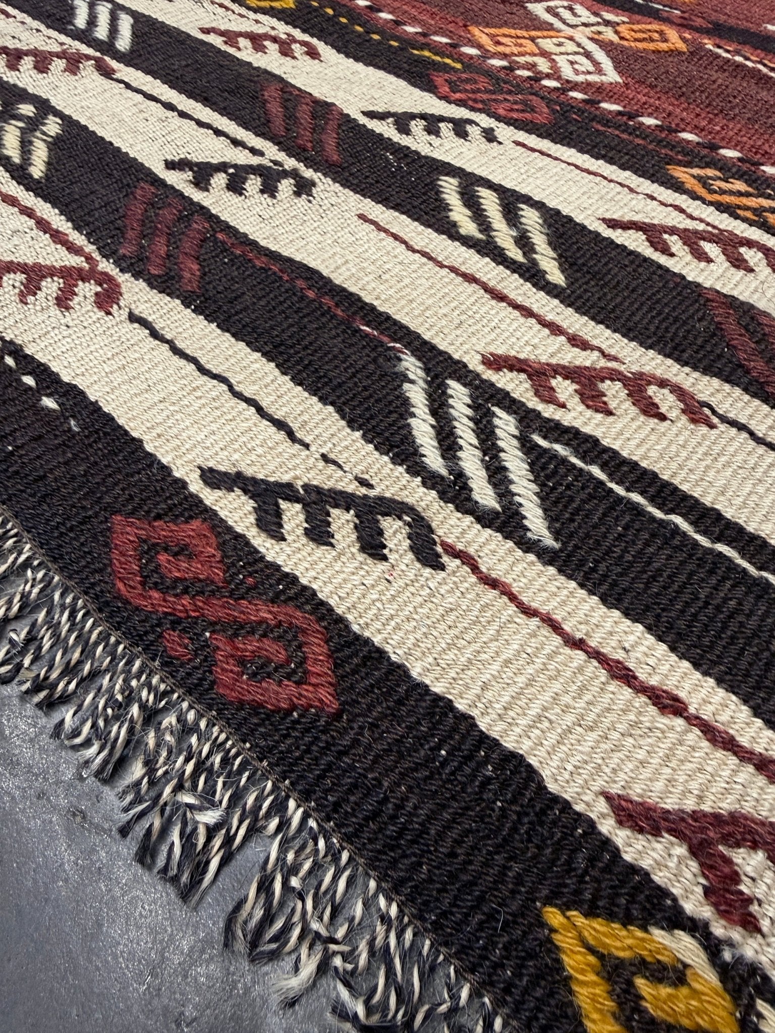 Close-up of a patterned fabric with geometric designs in brown, black, and beige. Vintage Kars kilim rug from Eastern Turkey, 6x8, with horizontal tribal bands in brown, ivory, rust, and charcoal geometric motifs.