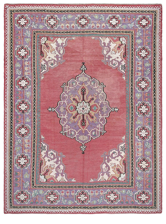 A rectangular traditional area rug with a dusty rose pink field, a central medallion, and a detailed border in muted purple, beige, and green tones.