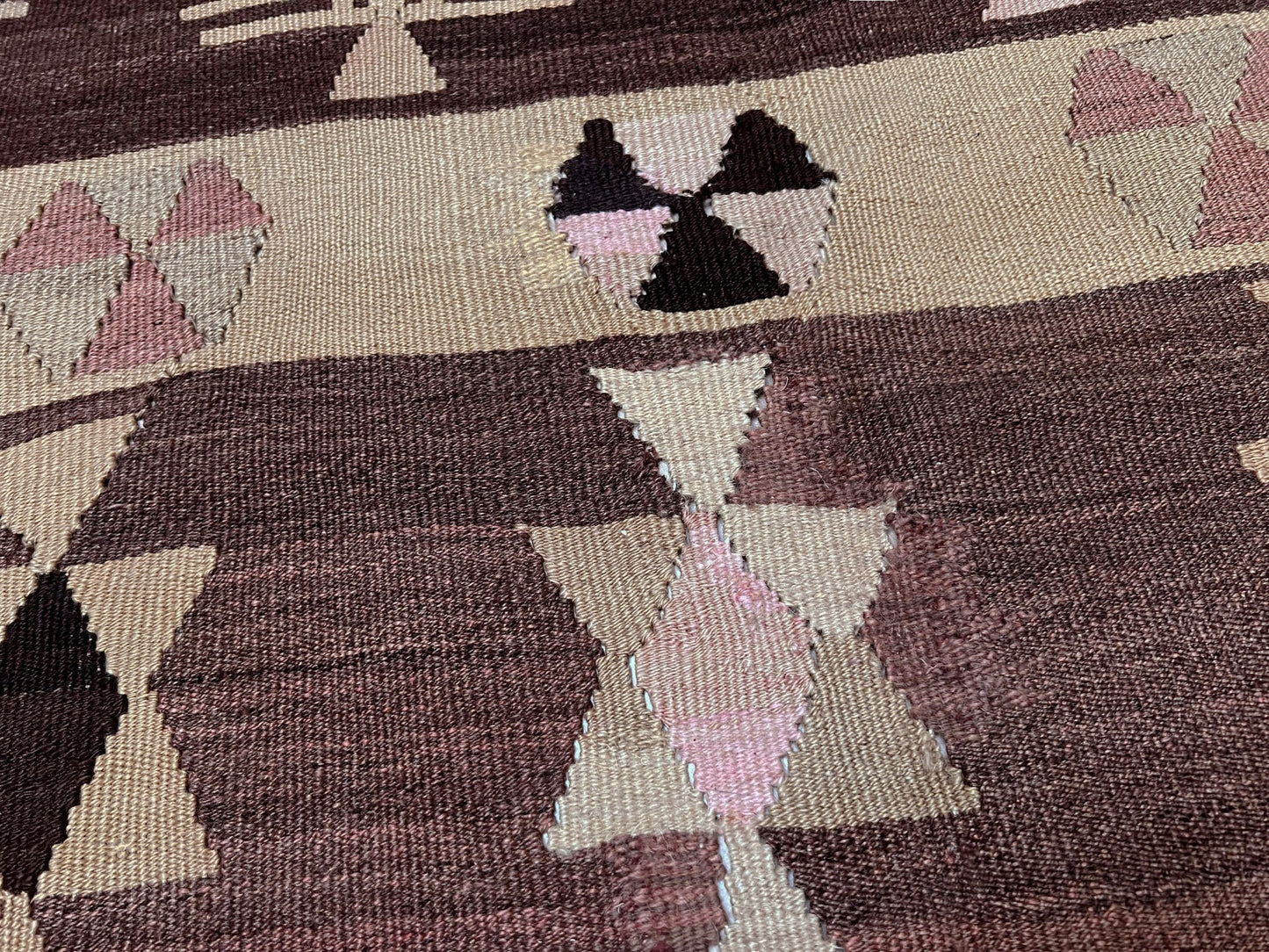Close-up of a woven textile with geometric patterns in brown, pink, and black on a beige background. Earthy Vintage Central Anatolian Turkish kilim rug, 6x8 with horizontal tribal bands and geometric motifs. 