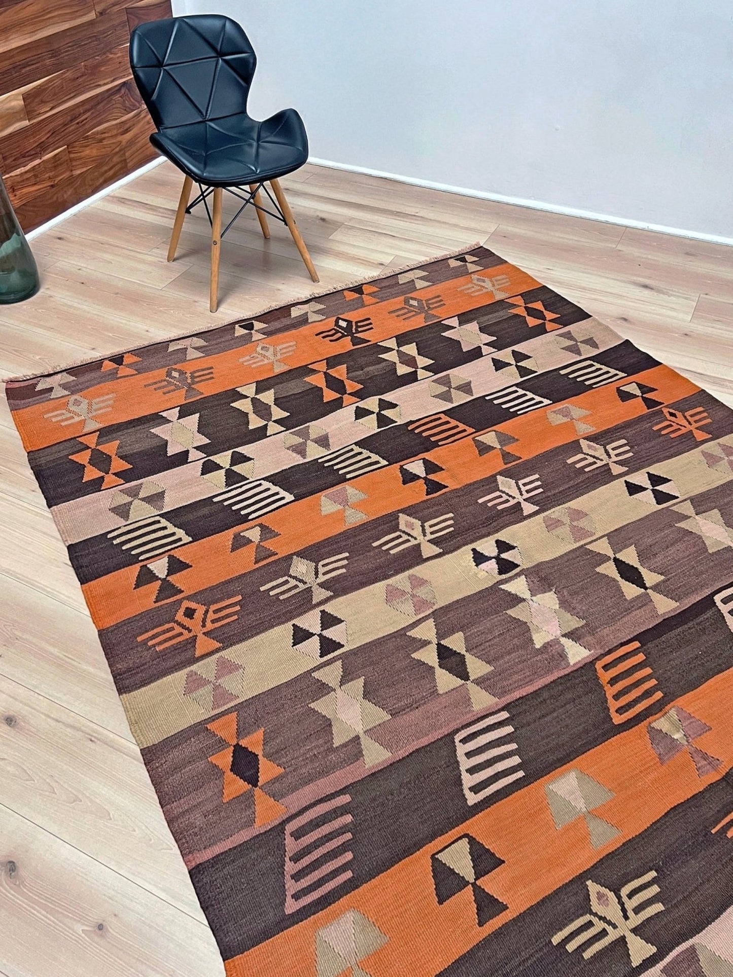 Geometric patterned rug on a wooden floor with a chair in the corner. Earthy Vintage Central Anatolian Turkish kilim rug, 6x8 with horizontal tribal bands and geometric motifs. 