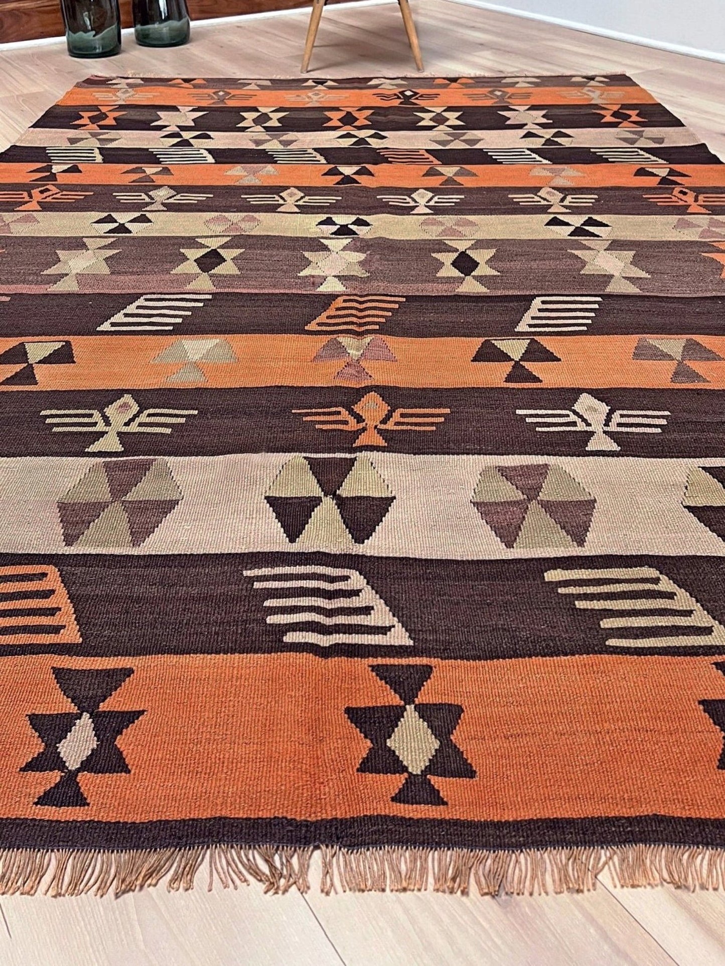 Patterned rug with geometric design on a wooden floor. Earthy Vintage Central Anatolian Turkish kilim rug, 6x8 with horizontal tribal bands and geometric motifs. 