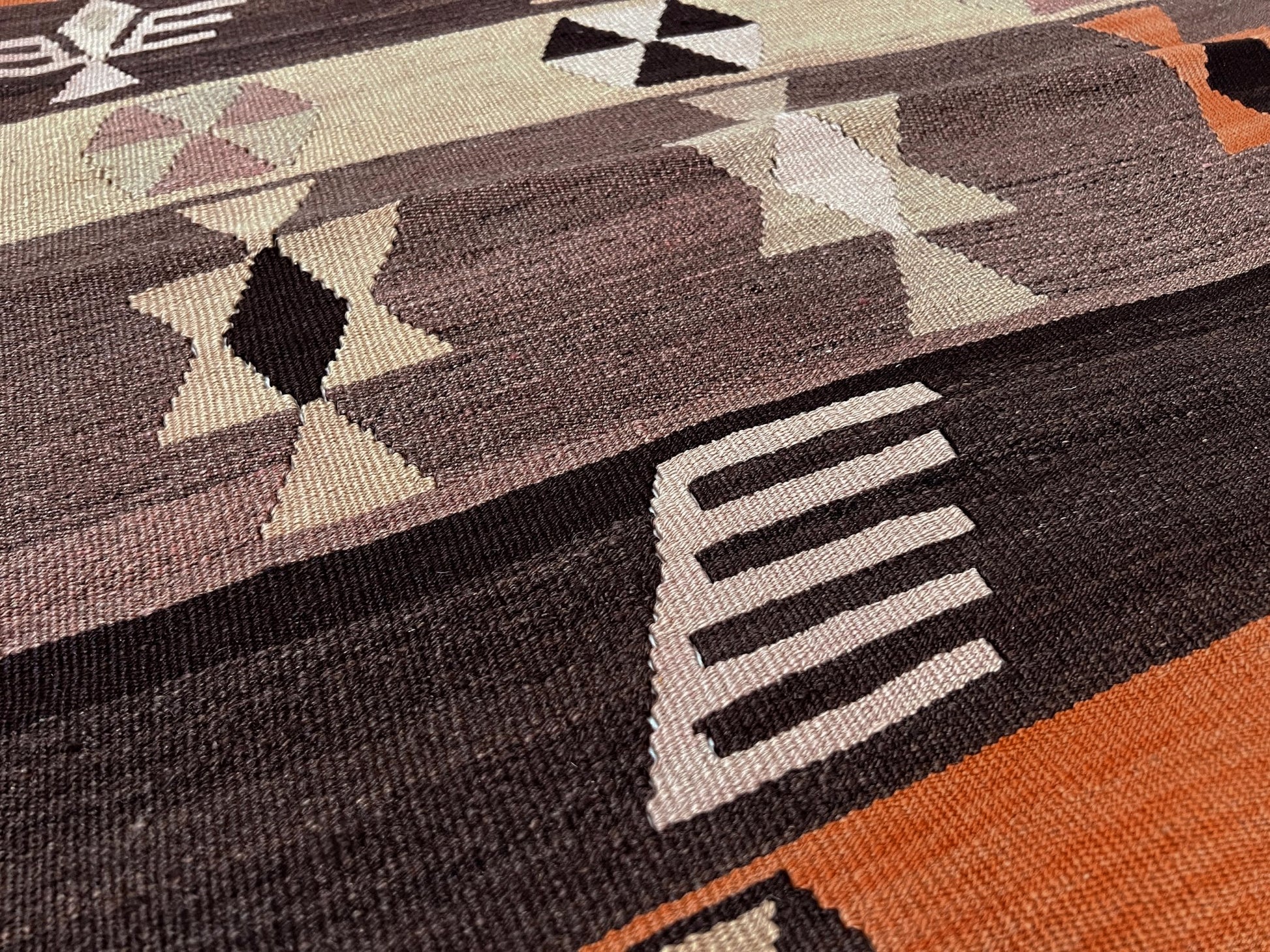 Close-up of a patterned rug with geometric designs in brown, black, and orange. Earthy Vintage Central Anatolian Turkish kilim rug, 6x8 with horizontal tribal bands and geometric motifs. 
