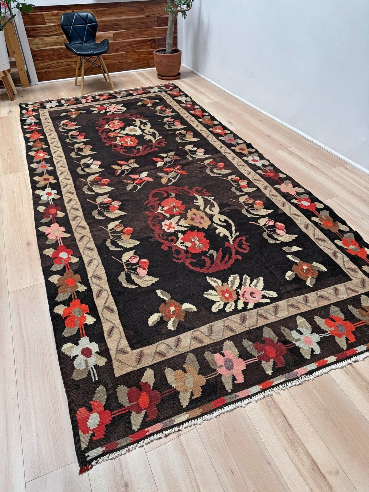 A long rectangular area rug with a dark brown to black field, featuring a central floral medallion and a decorative border, laid out on a light wood floor in a room.
