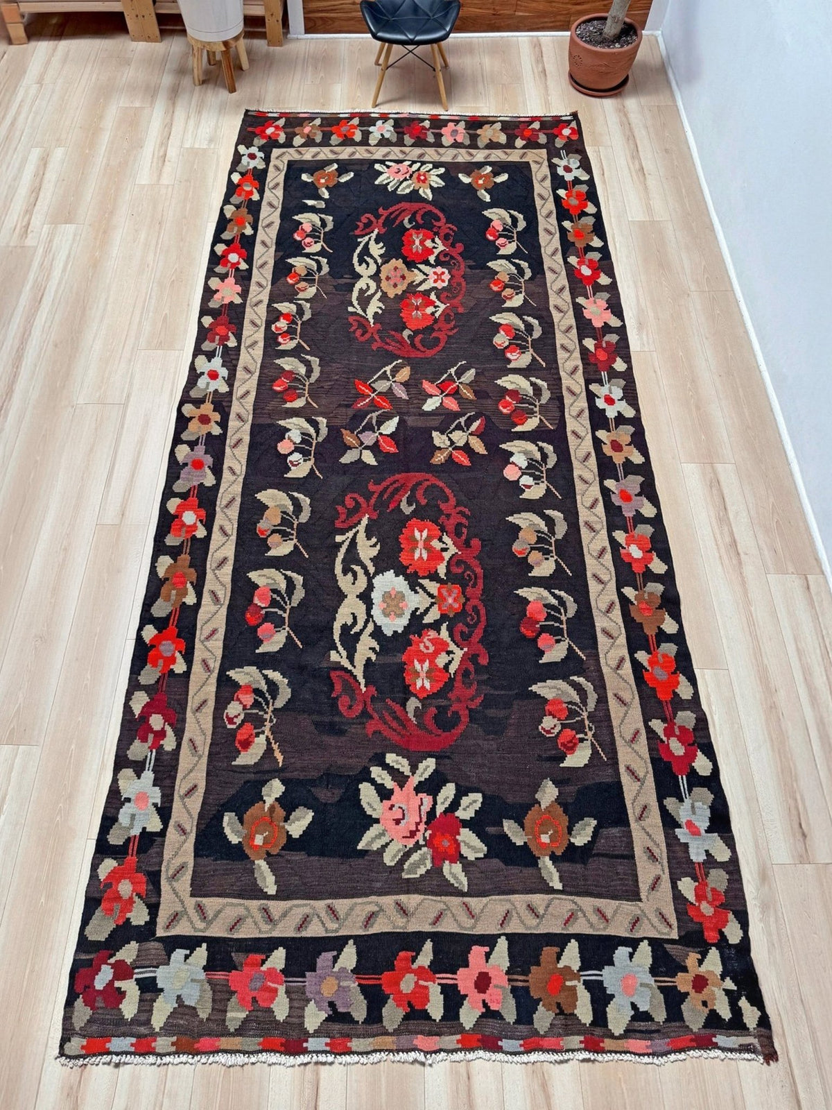 A long rectangular area rug with a dark charcoal-black background and a detailed floral pattern in red, beige, and muted green, laid out on a light wood floor.