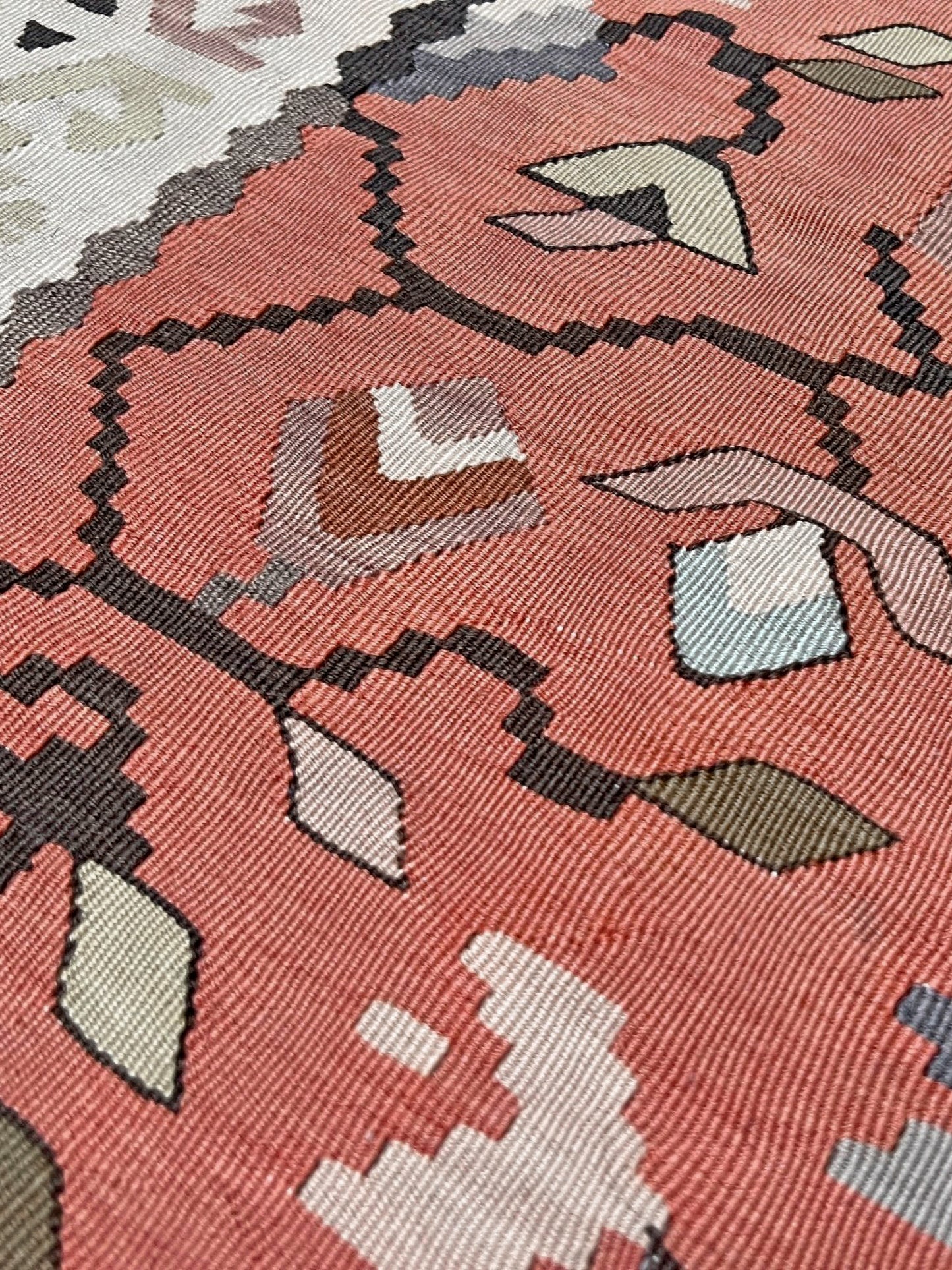 Close-up of a patterned fabric with geometric shapes on a pink background. Vintage Balkan Pirot Sharkoy kilim rug, 5x8 with faded geometric floral motifs in dusty coral pink, ivory, sage, and soft blue tones with natural abrash.