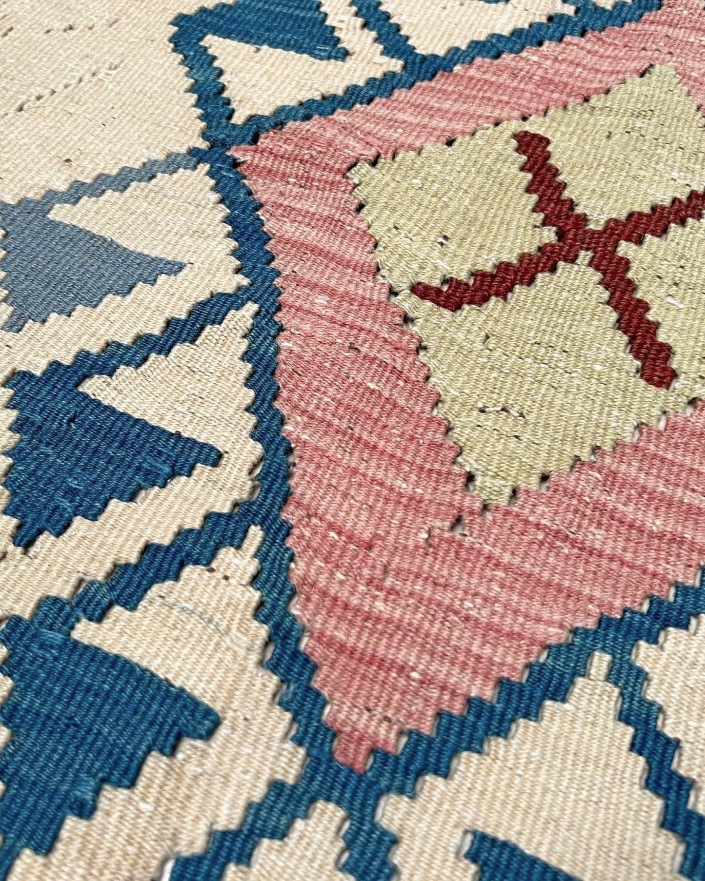 Decorative rug with geometric pattern featuring diamonds and cross symbols on a white background. Vintage Turkish kilim rug, 5x7, with ivory field, pink and blue tribal medallions, and geometric borders in brown and sage tones.