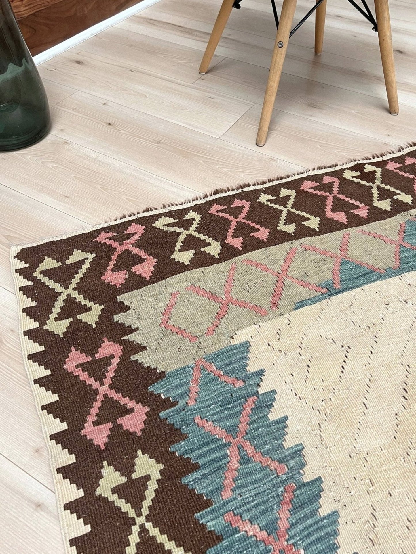 Decorative rug with geometric pattern featuring diamonds and cross symbols on a white background. Vintage Turkish kilim rug, 5x7, with ivory field, pink and blue tribal medallions, and geometric borders in brown and sage tones.