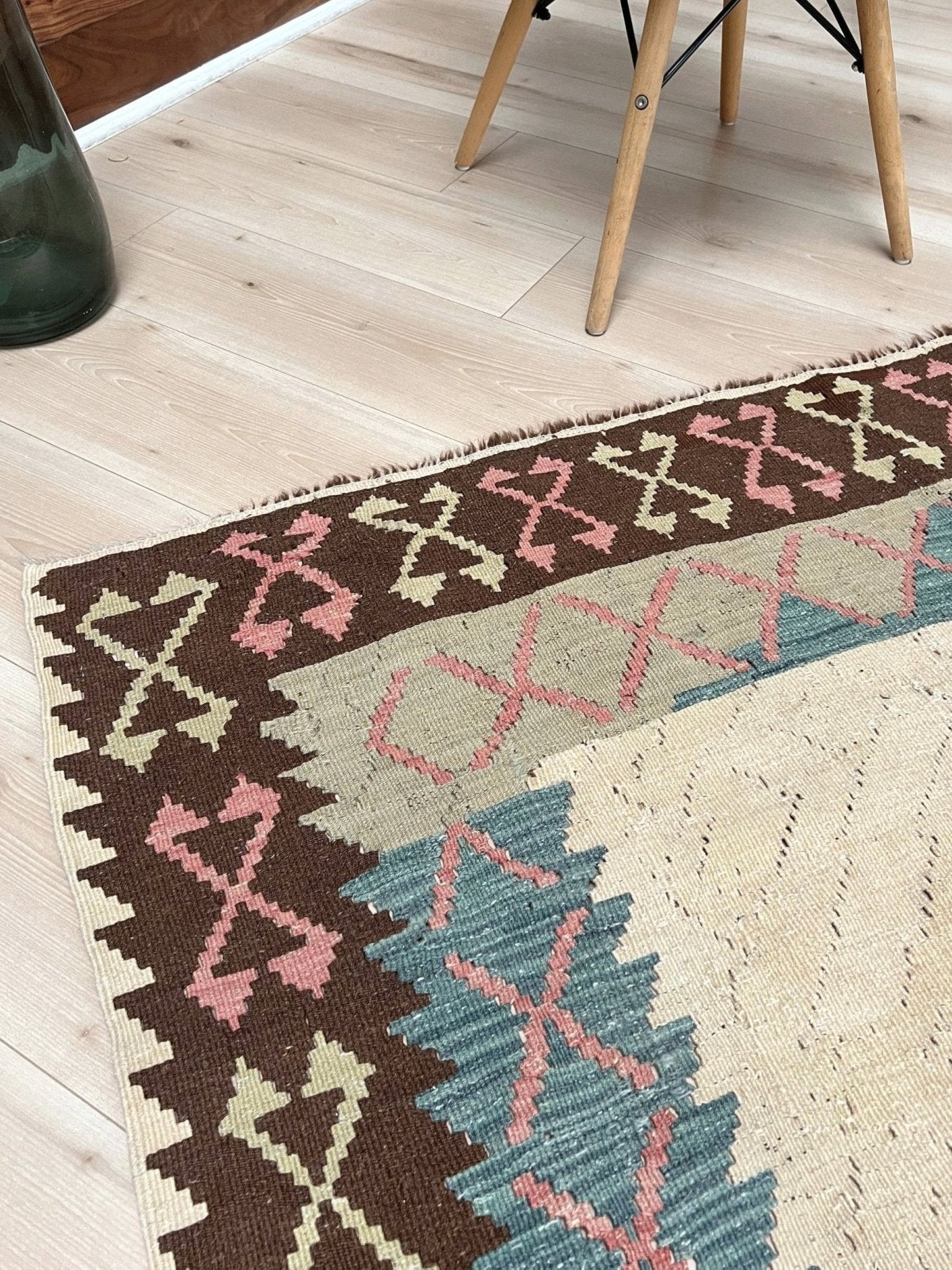 Decorative rug with geometric pattern featuring diamonds and cross symbols on a white background. Vintage Turkish kilim rug, 5x7, with ivory field, pink and blue tribal medallions, and geometric borders in brown and sage tones.