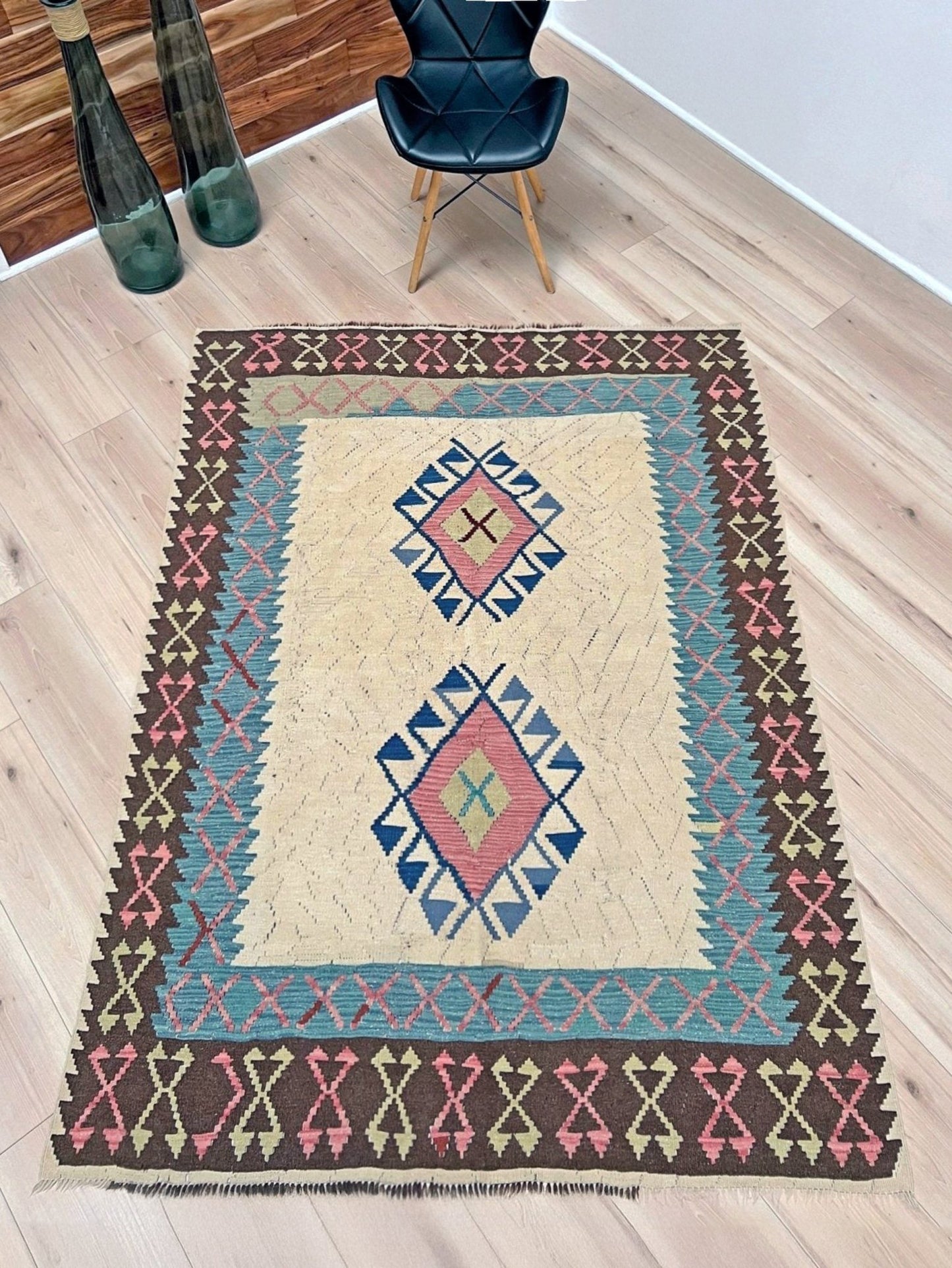 Decorative rug with geometric pattern featuring diamonds and cross symbols on a white background. Vintage Turkish kilim rug, 5x7, with ivory field, pink and blue tribal medallions, and geometric borders in brown and sage tones.