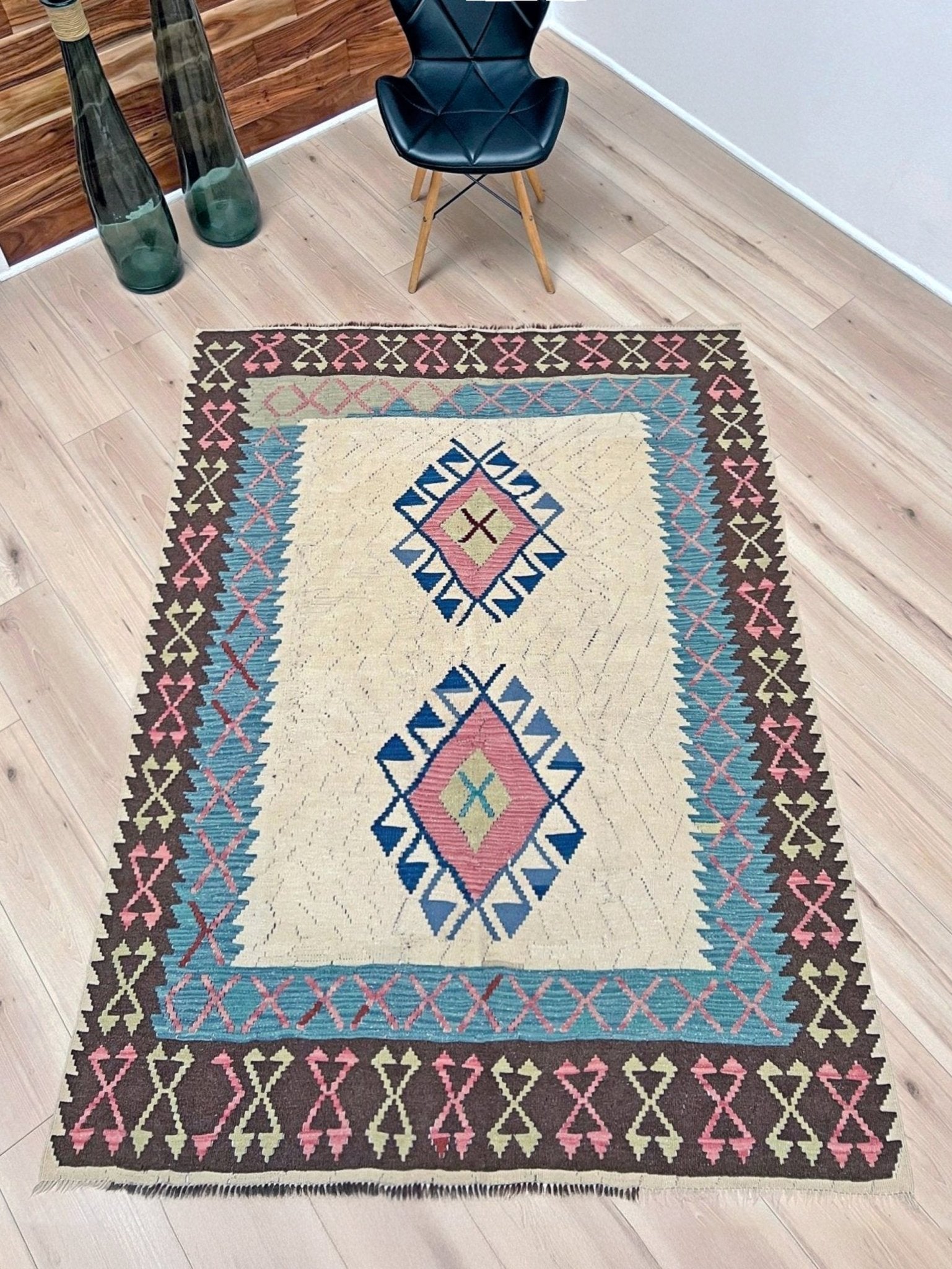 Decorative rug with geometric pattern on a wooden floor. Vintage Turkish kilim rug, 5x7, with ivory field, pink and blue tribal medallions, and geometric borders in brown and sage tones.