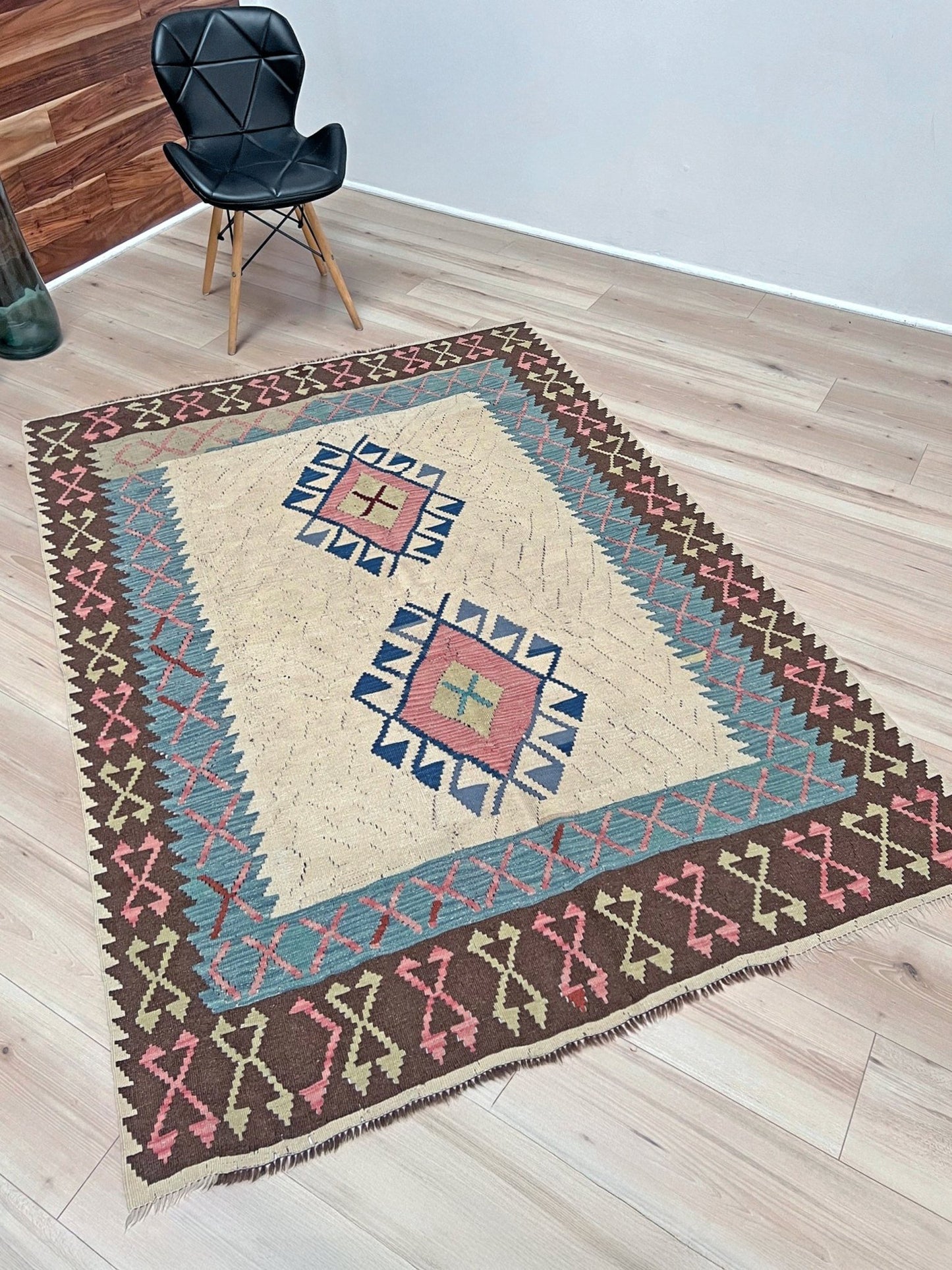 Decorative rug with geometric pattern featuring diamonds and cross symbols on a white background. Vintage Turkish kilim rug, 5x7, with ivory field, pink and blue tribal medallions, and geometric borders in brown and sage tones.