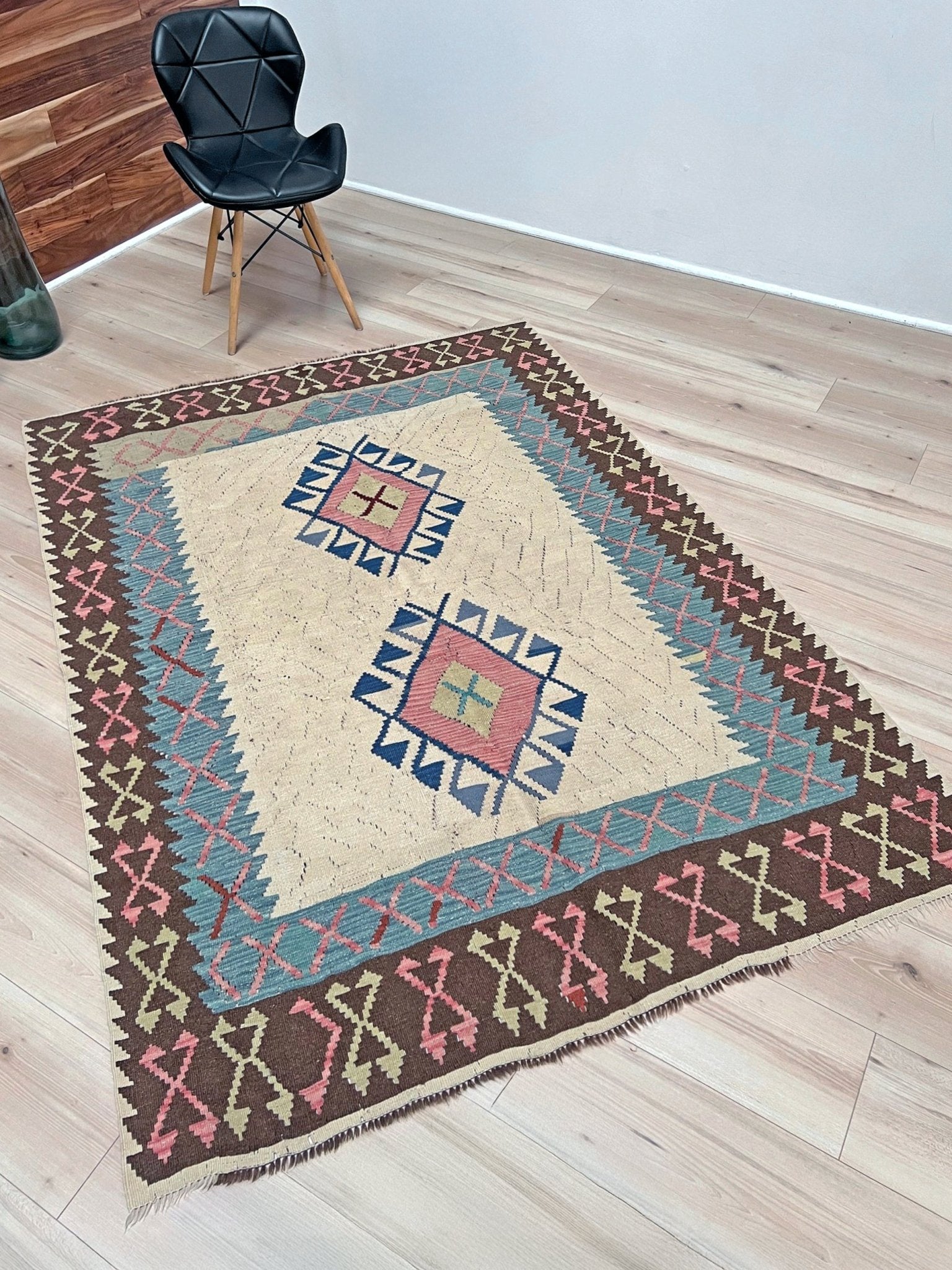 Decorative rug with geometric pattern featuring diamonds and cross symbols on a white background. Vintage Turkish kilim rug, 5x7, with ivory field, pink and blue tribal medallions, and geometric borders in brown and sage tones.