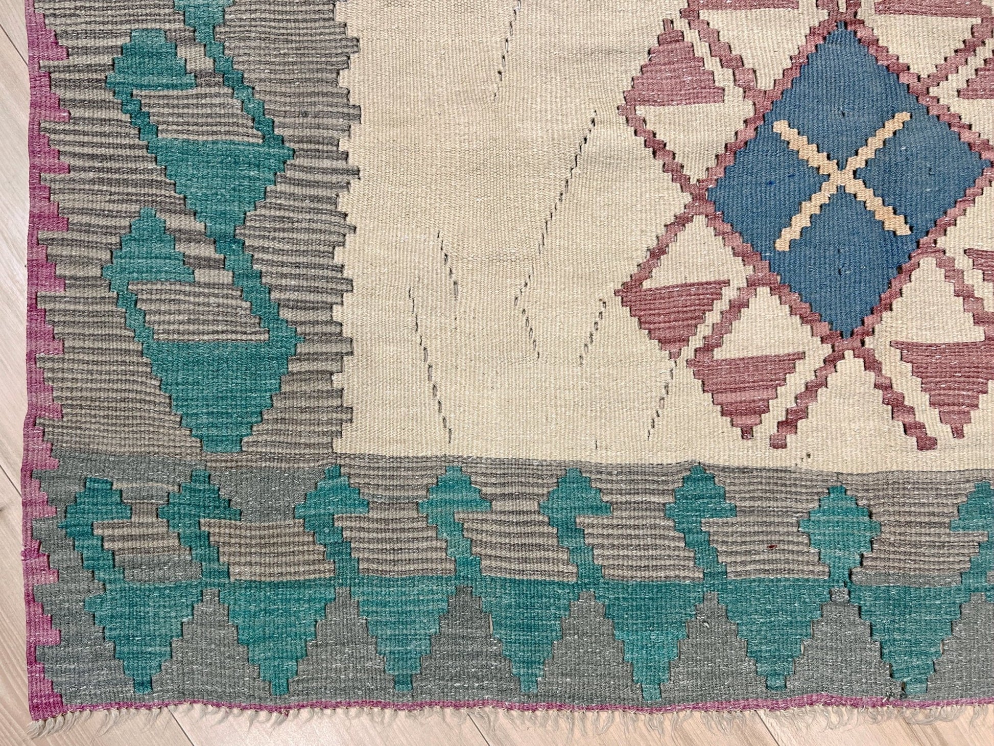 Geometric patterned rug with blue, gray, and purple colors on a wooden floor. Decorative rug with geometric pattern featuring diamonds and cross symbols on a white background. Vintage Turkish kilim rug, 5x7. 