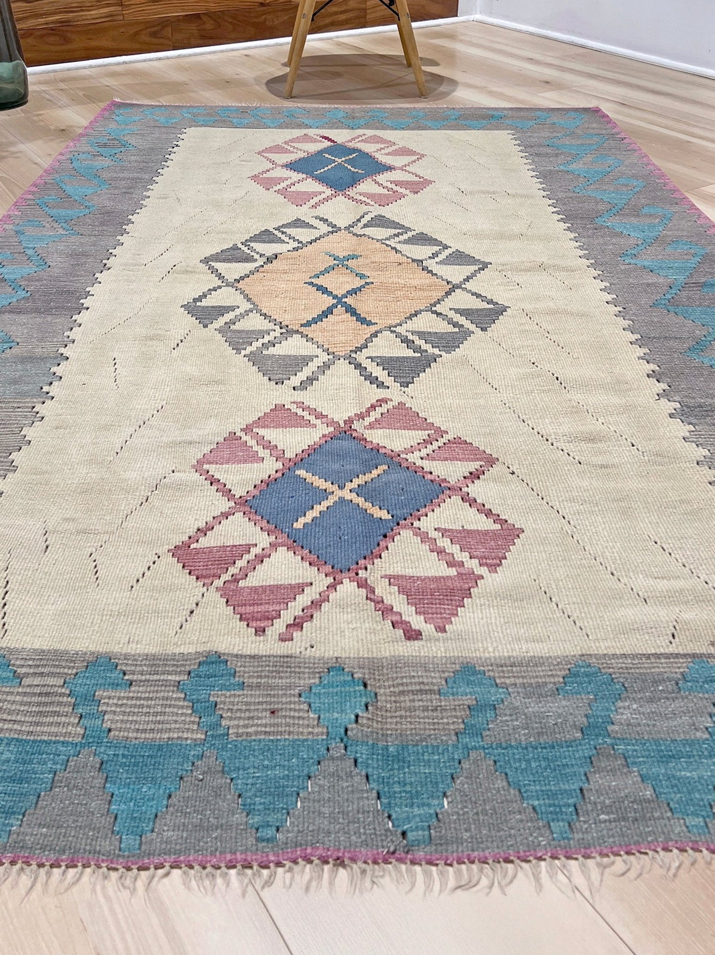 Decorative rug with geometric pattern featuring diamonds and cross symbols on a white background. Vintage Turkish kilim rug, 5x7. 