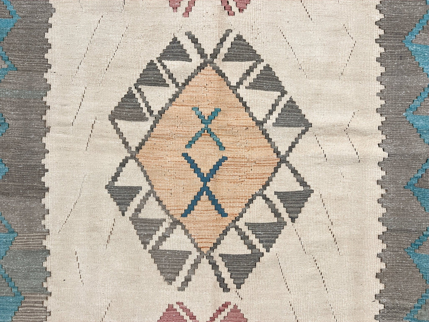 Close-up of a woven textile with geometric pattern on a beige background. Decorative rug with geometric pattern featuring diamonds and cross symbols on a white background. Vintage Turkish kilim rug, 5x7. 