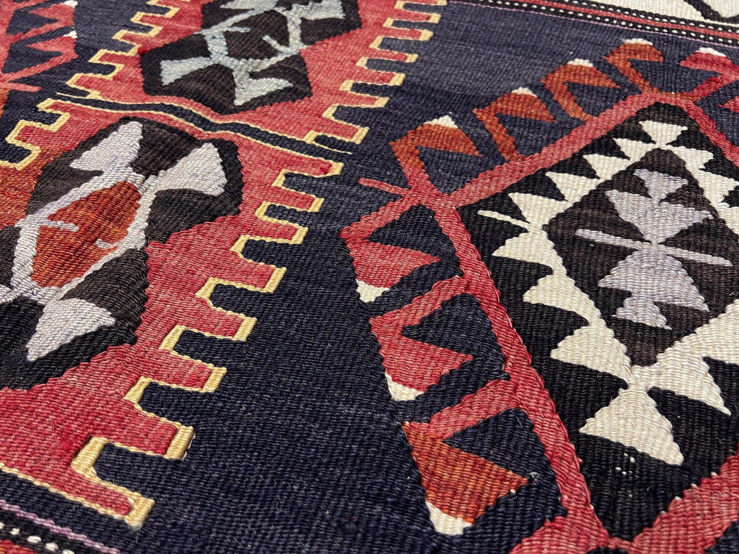 Close-up of a patterned fabric with red, black, and beige colors. 6x8 Vintage Karakecili Turkish kilim rug with bold tribal geometric motifs in charcoal, coral red, ivory, mustard, and soft gray, handwoven flatweave from the 1950s. 