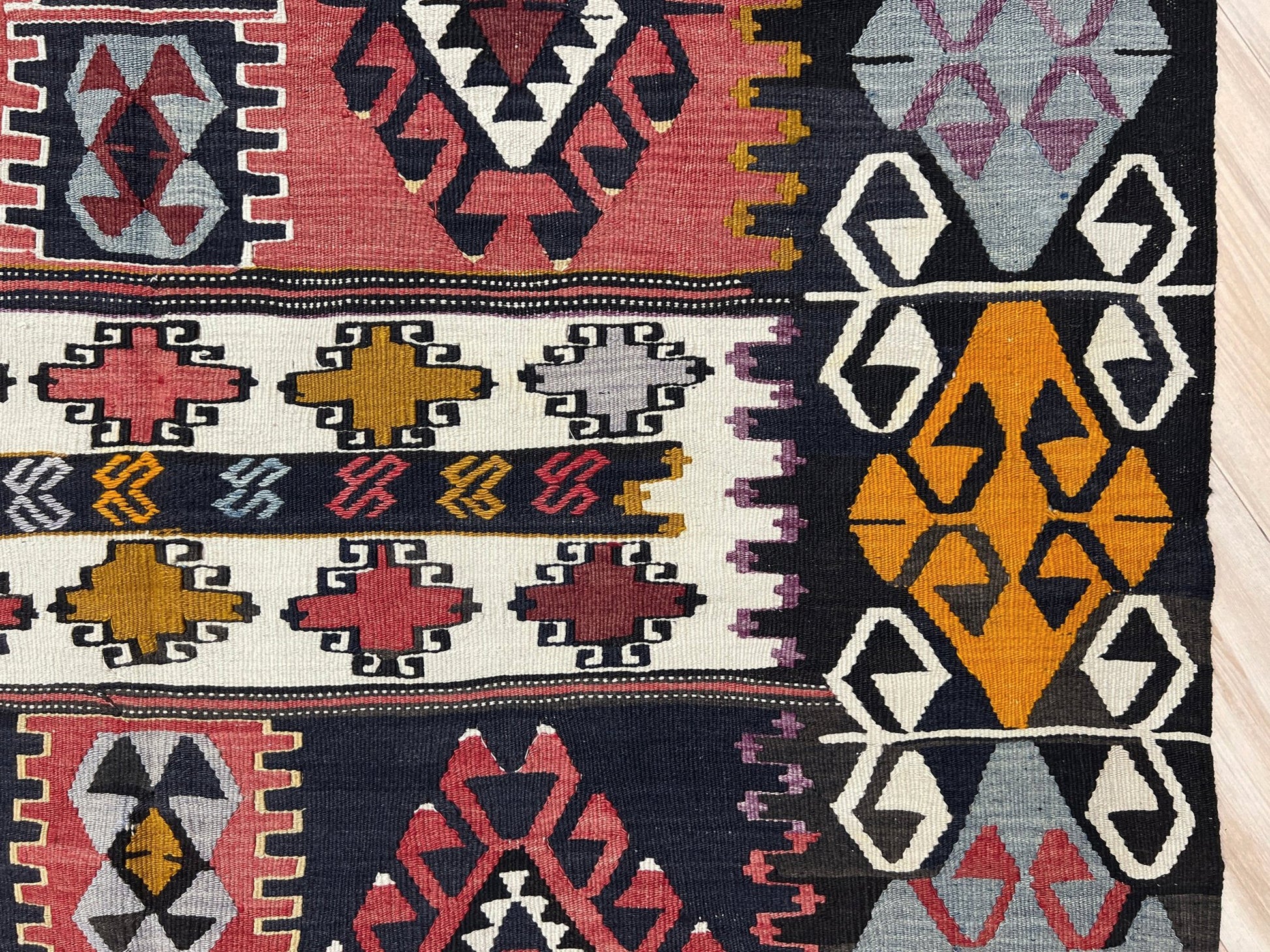 Close-up of a colorful patterned fabric with geometric designs. 6x8 Vintage Karakecili Turkish kilim rug with bold tribal geometric motifs in charcoal, coral red, ivory, mustard, and soft gray, handwoven flatweave from the 1950s. 