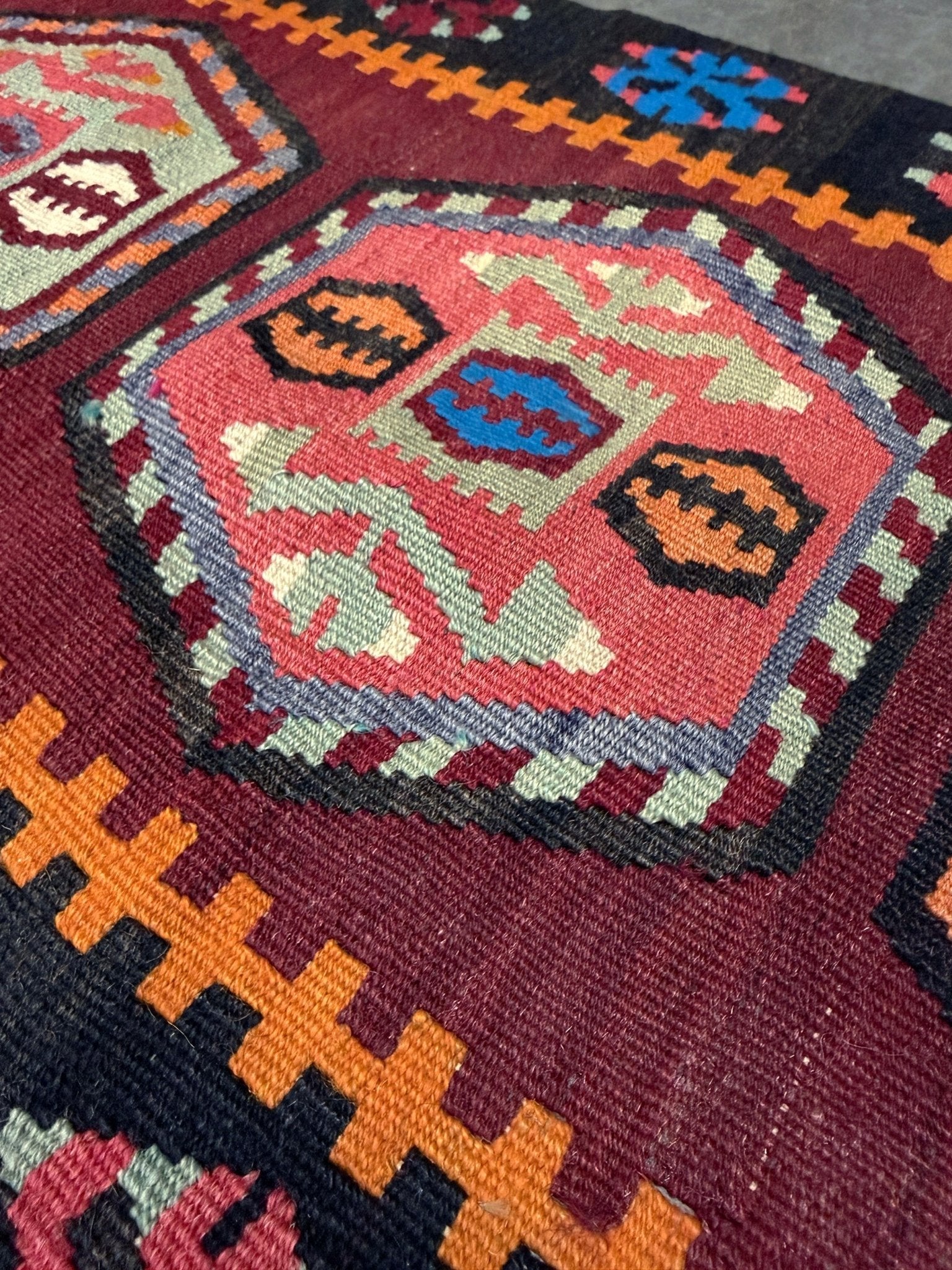Close-up of a patterned rug with geometric designs. Vintage Turkish Sarkisla mini kilim rug with berry red field, charcoal borders, colorful geometric medallions and tribal motifs, handmade wool flatweave accent rug 2x4 from Indigo Rugs Burlingame Bay Area.